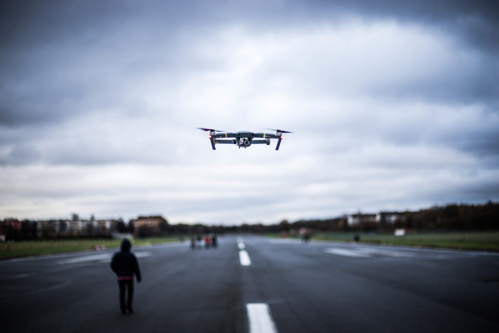 A person is walking down the street while flying a drone.