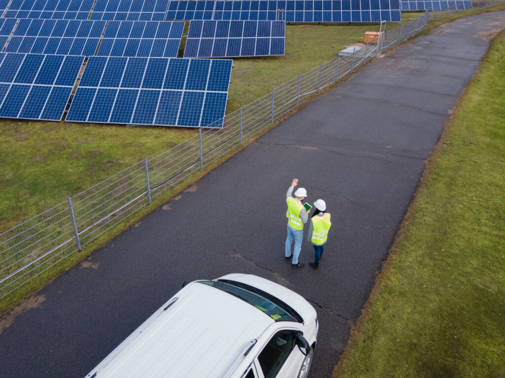 Two men standing next to a car in front of solar panels.