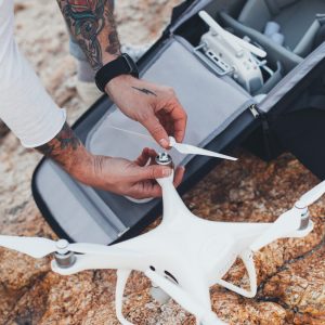 Hipster stock photographer with arm tattoos, adventurer and explorer of new tourist and travel destinations assembles drone with wings and propellers, after taking it out of professional backpack