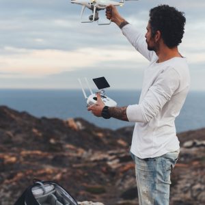 Professional drone pilot or stock photographer, prepares to fly high technology futuristic drone into air, sets up controls and remote connection. Ready to explore nature and cliffs from top